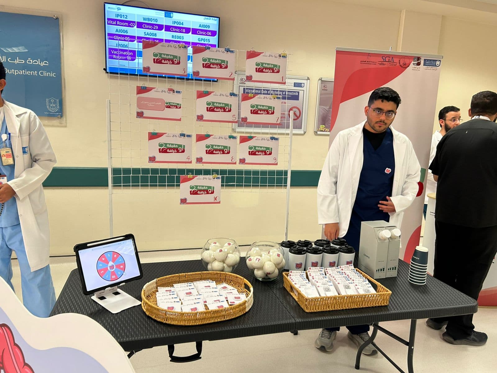 The interactive "Fact or Myth?" booth featuring a tablet-driven prize wheel, takeaway cards, and a medical-student volunteer in a white coat.